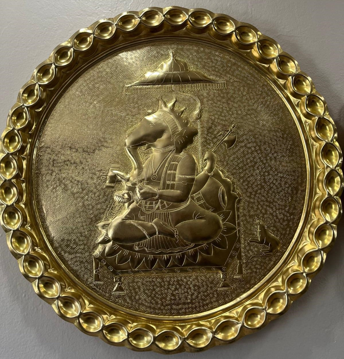 Decorative Brass plate with Lord Ganesha carving and intricate border on a gray background